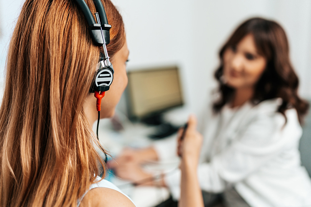 An redhead adult woman getting an auditory test at a hearing clinic.